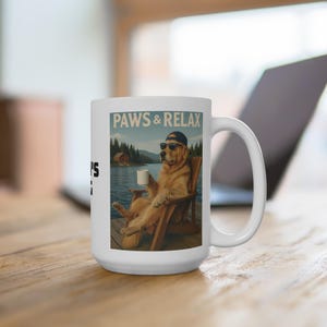 May include: White ceramic mug with a humorous graphic of a golden retriever wearing sunglasses and a cap, relaxing in a chair by a lake, holding a mug. The mug has the text "PAWS & RELAX" printed on it.