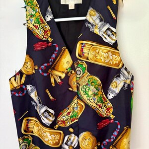 May include: A navy blue vest with a V-neck, featuring a repeating pattern of ornate gold, red, and green decorative objects. The vest has a black lining and is hanging on a white hanger.