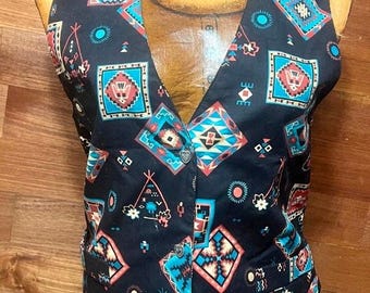 May include: A black vest with a Southwestern geometric pattern in teal, coral, and tan. The vest has a V-neck and three buttons down the front. The vest is displayed on a wooden mannequin.
