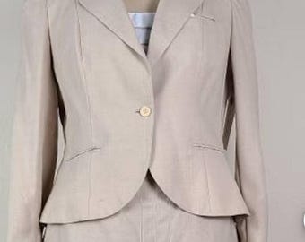 May include: A light beige two-piece suit displayed on a mannequin. The jacket has a single button closure, notched lapels, and subtle shoulder pads. The skirt features pleats. The suit is made of a light-coloured fabric.