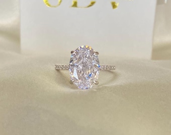 Peut inclure: Une bague en argent avec un grand diamant de forme ovale. La bague est sertie de petits diamants autour de la bande. La bague est sur un fond blanc avec une boîte qui dit "JDV Jewelry by Vanessa".
