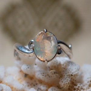 May include: A silver ring with a white opal gemstone. The ring has a delicate, curved band.