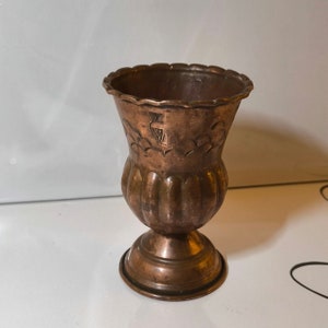 May include: A small, copper vase with a fluted body and a scalloped rim. The vase has an embossed design of a thistle and leaves.