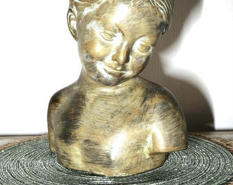 May include: A gold-toned ceramic bust sculpture of a young girl with her head tilted down. The sculpture is on a round, woven placemat.