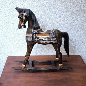 May include: A handcrafted wooden rocking horse with a dark brown finish. The horse features a detailed saddle, bridle, and mane. The rocking horse is mounted on a dark brown base and is a decorative item.