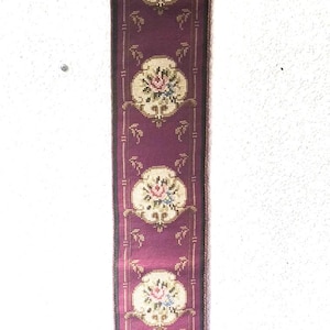 Könnte beinhalten: Ein dekorativer Wandbehang mit tiefviolettem Hintergrund und gestickten Blumenmedaillons. Der Behang ist mit einer metallischen Bordüre versehen und hat eine dekorative Metallober- und -unterseite. Die Gesamtlänge beträgt ca. 61 cm.