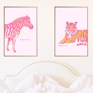 May include: Two framed art prints featuring animal illustrations. One print shows a zebra with pink and orange stripes, and the other depicts a tiger in a similar color scheme. Both are set against a light pink background.