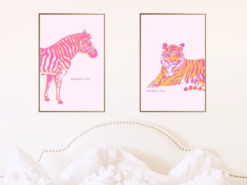 May include: Two framed art prints featuring animal illustrations. One print shows a zebra with pink and orange stripes, and the other depicts a tiger in a similar color scheme. Both are set against a light pink background.