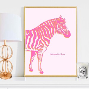 May include: A framed pink art print featuring a stylized zebra with pink and orange stripes. The artwork is set against a light pink background and framed in gold. The print includes the text "In Vogue Co | Etsy".