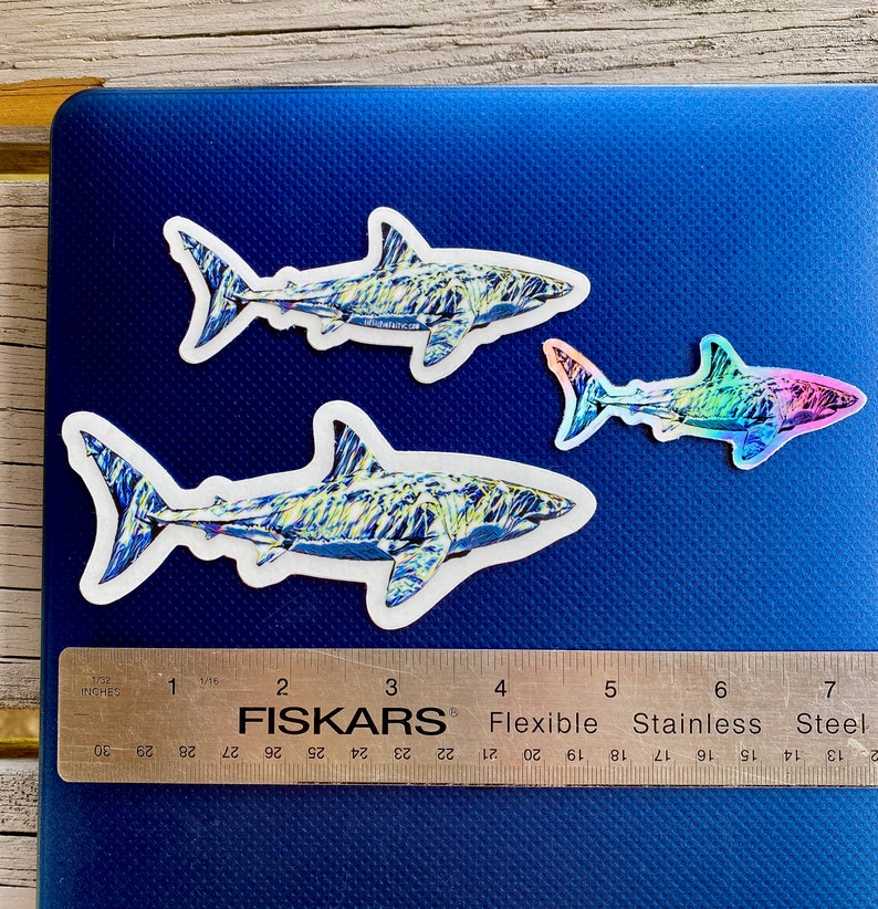 Three shark stickers on a laptop with ruler for sizing.