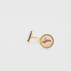 Op de afbeelding: Manchetknopen met een goudkleurige metalen basis. De ronde vlakken zijn van licht hout met een lasergeëtst orka-walvisontwerp. De achterkanten zijn zwart met een gouden rand, op een witte achtergrond.