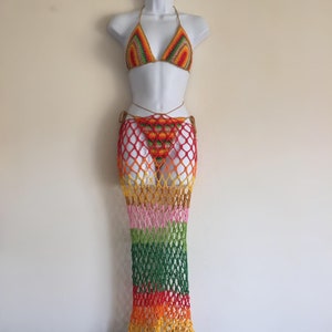 May include: A colorful crochet bikini set with a matching skirt. The bikini top and bottom are in a rainbow pattern, with a halter top design. The skirt is a net-like design, with a gradient of colors from orange to pink.