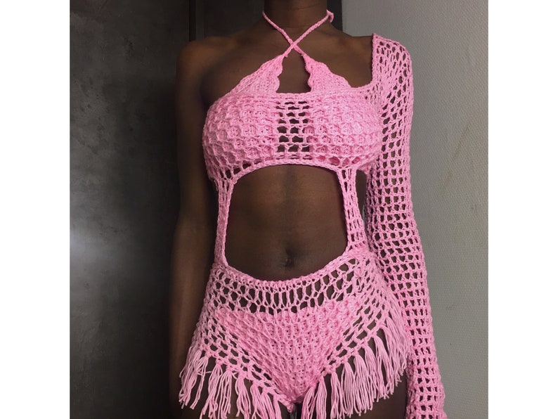 Peut inclure: Combinaison de bain en crochet rose avec un haut halter et une manche longue. La combinaison de bain a un design d&eacute;coup&eacute; et des d&eacute;tails en frange.