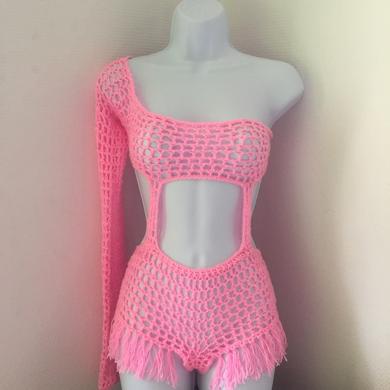 Peut inclure: Un maillot de bain une pi&egrave;ce en crochet rose avec une manche longue d'un c&ocirc;t&eacute; et une bordure en franges. Le maillot de bain a une d&eacute;coupe au niveau de la taille et de la poitrine.