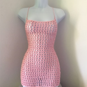 May include: A pink crochet dress with a loose, open weave. The dress has a scoop neck and thin straps.