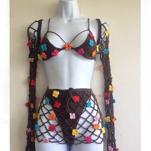 May include: A brown crochet bikini set with colorful flower accents. The set includes a bra top, a skirt, and a long-sleeved top.