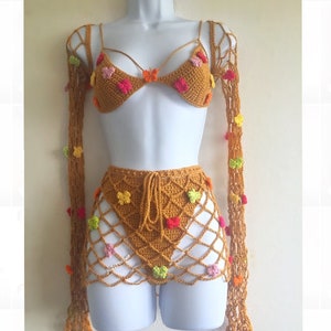 May include: A crocheted bikini set with a mustard yellow base color and colorful flower accents. The set includes a halter top with long sleeves, a matching bottom, and a skirt.