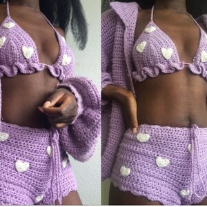 May include: A purple crochet cardigan, bikini top, and shorts set with white heart accents. The set is made of soft, lightweight yarn and is perfect for a casual, relaxed look.