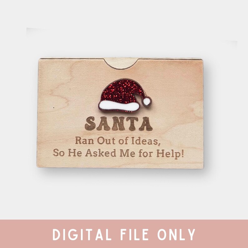 Pu&ograve; includere: Una scatola regalo in legno con un cappello di Babbo Natale rosso glitterato in cima. La scatola ha il testo "SANTA Ran Out of Ideas, So He Asked Me for Help!" stampato su di essa.