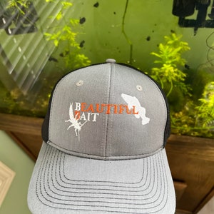 May include: A gray and black trucker hat with the words "BEAUTIFUL BAIT" in orange and white. The hat features a fish graphic and a curved brim.