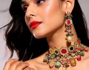 Op de afbeelding: Een gouden chokerketting met een veelkleurig geometrisch ontwerp en hangende edelstenen. De ketting heeft rode, groene, blauwe en gele stenen.
