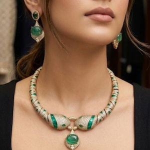 May include: A luxurious necklace and earring set featuring emerald green gemstones and sparkling white diamonds. The necklace has a snake-like design with a large pendant. The earrings have a matching design. The jewelry is set in gold.