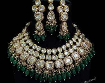May include: A gold and green Indian bridal necklace and earrings set with large, clear, faceted stones and green beads. The necklace has two rows of stones and the earrings are teardrop shaped.