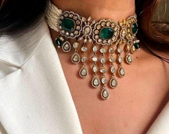 May include: A gold choker necklace with a row of white pearls and a dangling design of emerald green and clear stones.