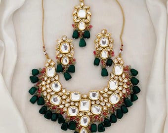 May include: A gold necklace set with a green and pink stone design. The necklace features a large pendant with multiple layers of stones and a smaller pendant with a single layer of stones. The earrings are similar in design to the smaller pendant.