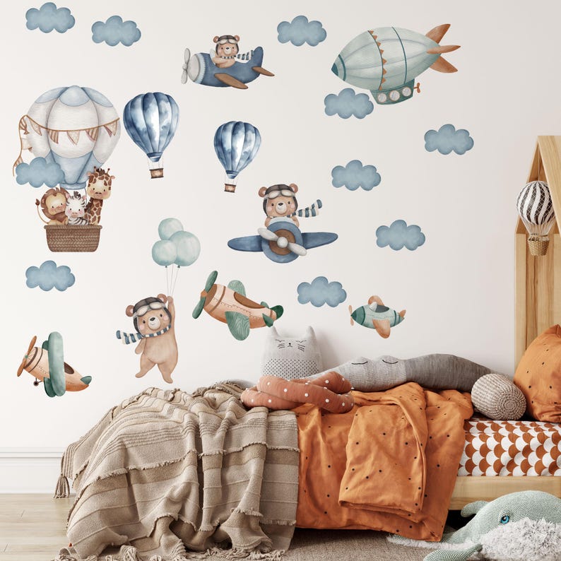 May include: A set of wall decals featuring watercolor illustrations of teddy bears in aviator gear, flying airplanes, hot air balloons, and a blimp. The collection includes various blue clouds, a large balloon with a lion, zebra, and giraffe.