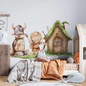 May include: A watercolor illustration of a Viking warrior with a bow and arrow, a stone Viking helmet, and a small wooden house with a green roof. The illustration is on a white wall in a child's bedroom with a bed, pillows, and a rug.