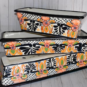 May include: Three ceramic planter boxes with black trim and colorful floral designs. The planters are stacked on top of each other, with the largest planter on the bottom and the smallest planter on top.