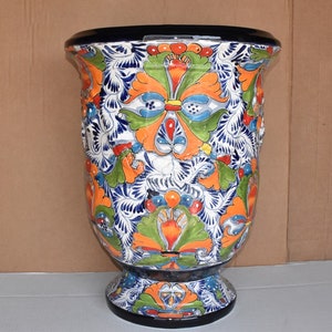May include: A large, hand-painted ceramic planter with a traditional Mexican Talavera design. The planter features a white background with intricate floral patterns in shades of blue, green, orange, and red.