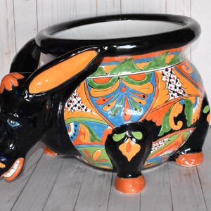 May include: A black ceramic planter shaped like a donkey with colorful Mexican Talavera style painted designs. The planter has a wide opening at the top for planting.
