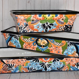 Pu&ograve; includere: Tre vasi da fiori in ceramica colorati con bordi neri e motivi floreali. I vasi sono impilati uno sopra l'altro, con il vaso pi&ugrave; grande in basso e il pi&ugrave; piccolo in alto.