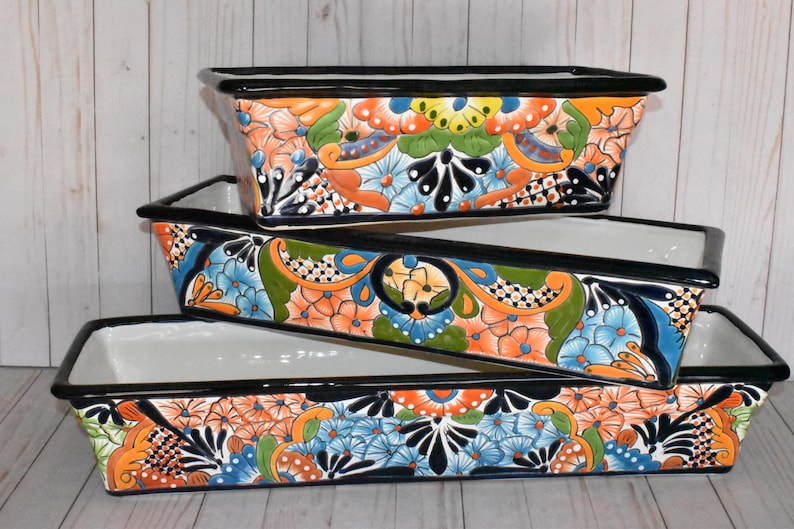 Pu&ograve; includere: Tre vasi da fiori in ceramica colorati con bordi neri e motivi floreali. I vasi sono impilati uno sopra l'altro, con il vaso pi&ugrave; grande in basso e il pi&ugrave; piccolo in alto.