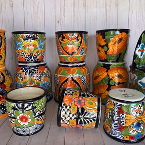 May include: A collection of vibrantly painted ceramic planters. The planters feature intricate floral and geometric designs in a variety of colors, including orange, blue, green, and yellow. The planters are of various sizes and shapes, suitable for indoor or outdoor use.