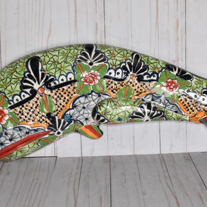 May include: A ceramic whale wall hanging with a colorful floral and geometric pattern in shades of green, orange, red, black, and white.