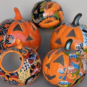 May include: A collection of five ceramic pumpkin decorations. The pumpkins are orange with carved triangular faces. Some have colorful floral and patterned designs. The pumpkins vary in size and shape, perfect for Halloween.