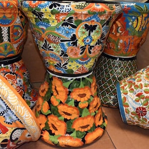 May include: Four colorful ceramic planters with intricate floral designs. The planters are in various sizes and shapes, with a mix of orange, blue, green, and white colors.