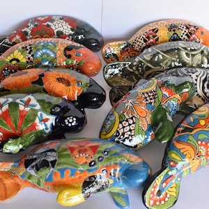 May include: A collection of ten hand-painted ceramic manatee figurines. Each manatee is decorated with colorful floral patterns and intricate details. The manatees are arranged in a circle, with their tails pointing outwards.