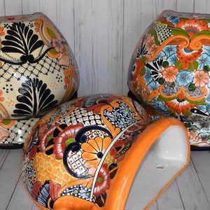 May include: Three hand-painted ceramic planters with vibrant floral designs in orange, blue, and green. The planters have a bulbous shape and a black base. The designs include intricate patterns and details, showcasing a traditional style.