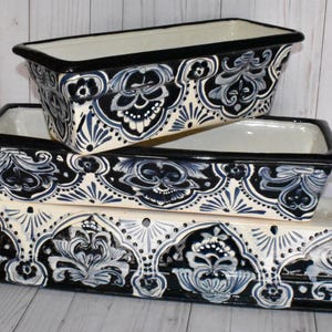 May include: Three black and white ceramic planters with a floral design. The planters are stacked on top of each other, with the largest planter on the bottom and the smallest planter on top.