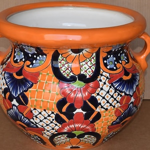 May include: A large, orange ceramic planter with two handles. The planter is decorated with a colorful floral pattern in shades of blue, red, green, and white.