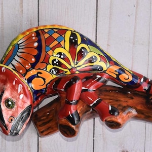 May include: A colorful ceramic chameleon figurine with intricate details, painted in shades of red, yellow, blue, and green. The chameleon is perched on a branch, with its tail curled around the branch.