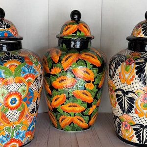May include: Three decorative ceramic jars with lids. The jars feature vibrant hand-painted designs in orange, blue, green, and black. The lids are black with a small knob. The jars are likely used for storage or decoration.
