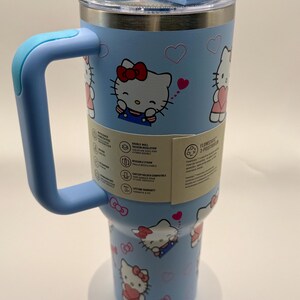 Pu&ograve; includere: Un bicchiere termico azzurro con manico, con un design di Hello Kitty. Il bicchiere ha un coperchio trasparente e un manico azzurro. Il design include illustrazioni di Hello Kitty, cuori e fiocchi. Capacit&agrave; di circa 887 ml.