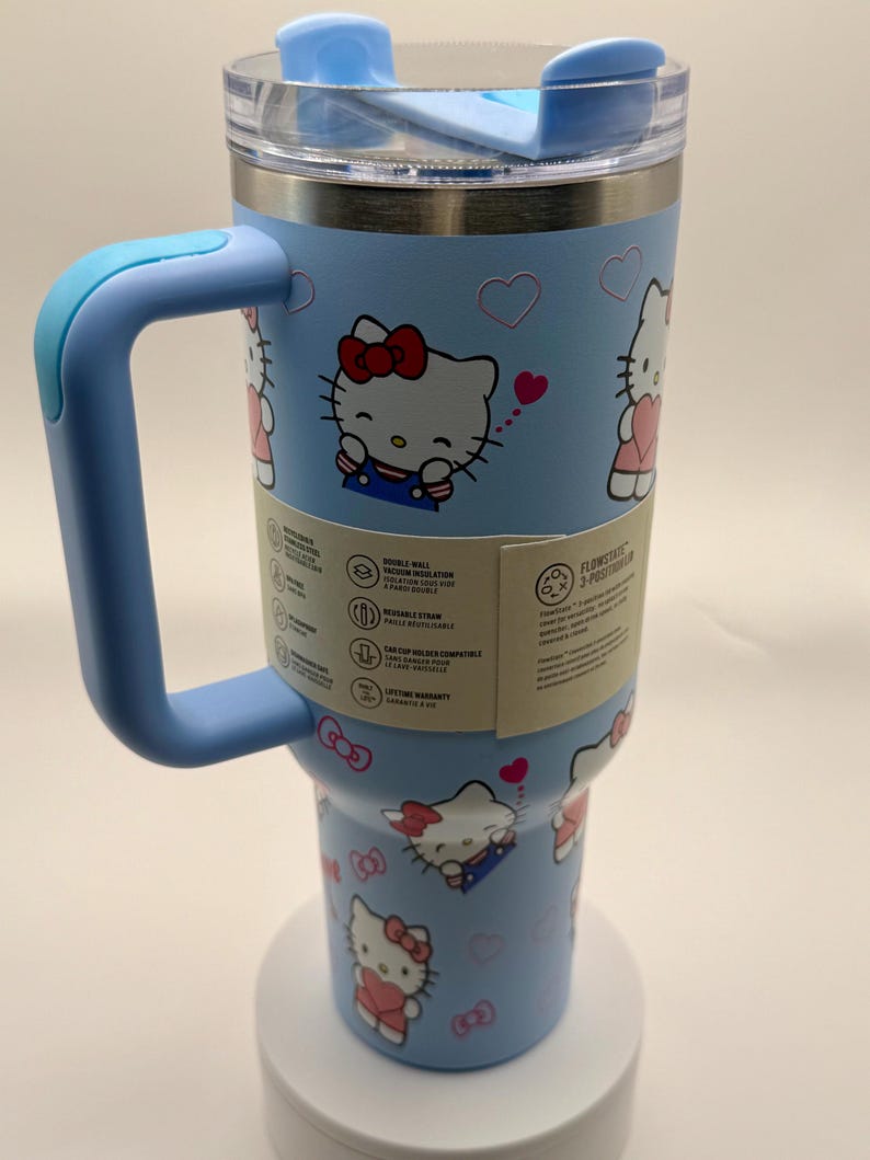 Pu&ograve; includere: Un bicchiere termico azzurro con manico, con un design di Hello Kitty. Il bicchiere ha un coperchio trasparente e un manico azzurro. Il design include illustrazioni di Hello Kitty, cuori e fiocchi. Capacit&agrave; di circa 887 ml.