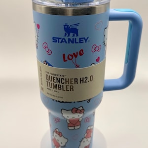 Pu&ograve; includere: Bicchiere Stanley Quencher H2.0 azzurro con manico, con design Hello Kitty. Il bicchiere ha una capacit&agrave; di 1,18 L. Il coperchio e il manico sono anch'essi azzurri.