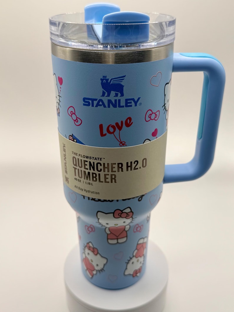 Pu&ograve; includere: Bicchiere Stanley Quencher H2.0 azzurro con manico, con design Hello Kitty. Il bicchiere ha una capacit&agrave; di 1,18 L. Il coperchio e il manico sono anch'essi azzurri.